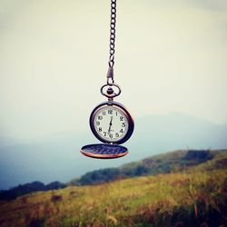 Pocket watch hanging over field against clear sky