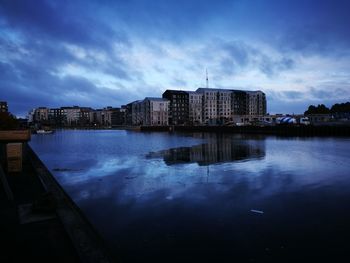 Buildings by lake against blue sky at dusk