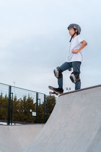 Teenage skater in protective gear riding skateboard during weekend in skate park and looking away