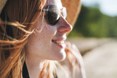 Close up portrait of red haired young woman in straw hat and sunglasses on sunset landscape