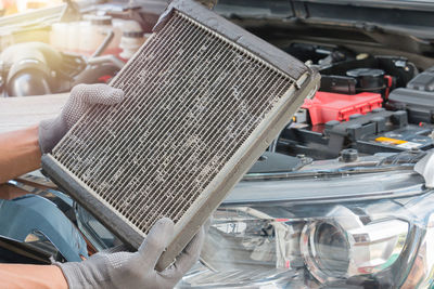 Close-up of mechanic hand holding vehicle part by car engine