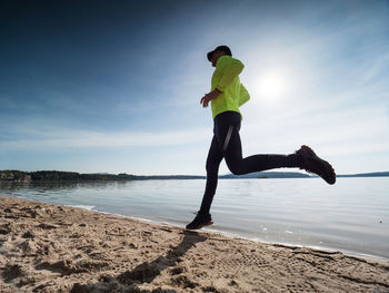 Yellow jersey and black leggings man run on the sandy beach early morning in summer holiday resort