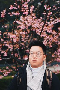 Portrait of young man standing by cherry blossom