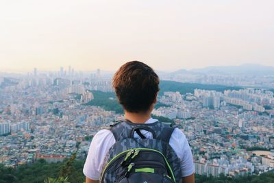 Rear view of man looking at cityscape against sky