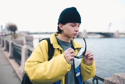 Handsome guy teenager boy 18-19 year old wear knit hat and trendy winter jacket posing at city view