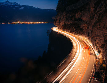 Light trails on road by mountain against sky at night