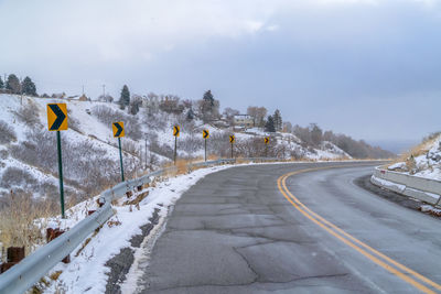 Snow covered road by trees against sky