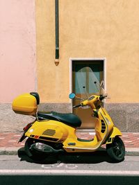 Yellow motor scooter parked in a street in front of a yellow wall with sunlight and copy space 