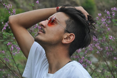 Side view of young guy wearing white t-shirt and sunglasses with passing his hand through his hair 