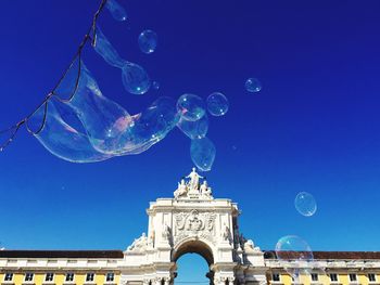 Low angle view of bubbles with rua augusta arch against clear blue sky