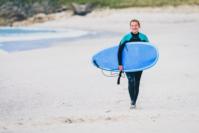 Portrait of woman carrying surfboard walking at beach