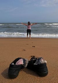 Rear view of woman standing with arms outstretched at beach against sky