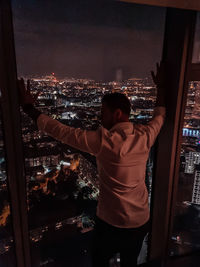 Rear view of man looking at illuminated city buildings