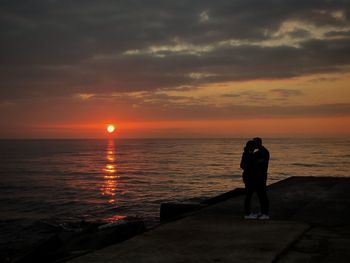 Rear view of man standing at beach during sunset