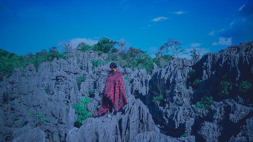 Rear view of woman standing on rock against blue sky