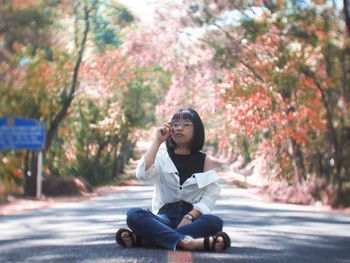 Woman sitting on road against trees