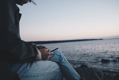 Midsection of woman using mobile phone while sitting at lakeshore