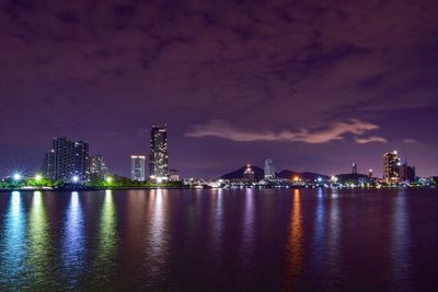 Illuminated buildings by river against sky at night