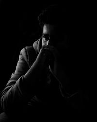 Young man sitting with hands clasped against black background