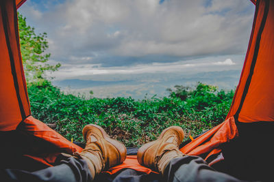 Low section of person relaxing in tent against sky