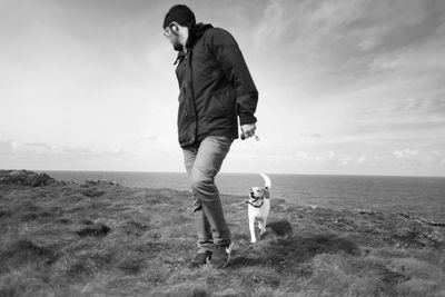 Full length of man walking with dog on cliff against sea