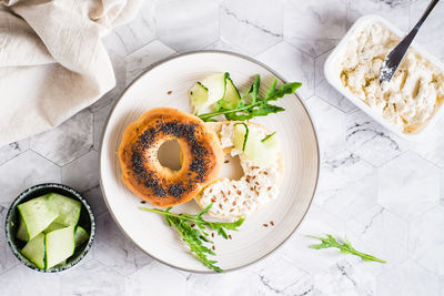 Bagel sandwich with cream cheese, cucumber and arugula on a plate on the table