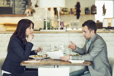 Side view of businessman with female colleague discussing paperwork at restaurant table