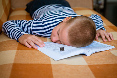 Boy fell asleep while lying on the couch reading a book or doing homework.