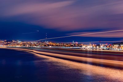 Illuminated light trails on city against sky at night