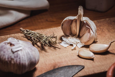 Garlic head and cloves on wooden board next to rosemary branches