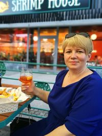 Portrait of smiling woman holding drink on table in restaurant