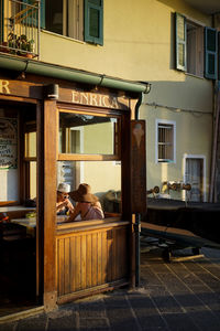 Rear view of woman sitting on table by building