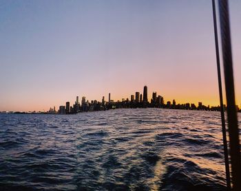 Sea and buildings against clear sky during sunset