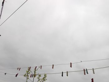 Low angle view of birds perching on cable against sky