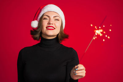 Smiling woman holding sparkler against red background