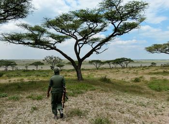 Rear view of man walking on field against sky