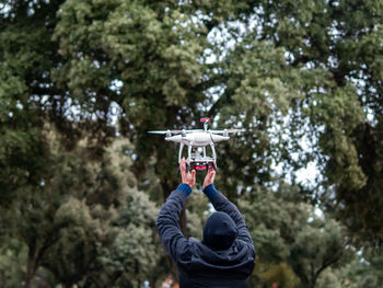 Rear view of man flying drone against trees