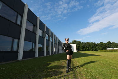 Full length of fashionable woman standing on field by building against sky