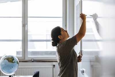 Side view of female teacher writing on whiteboard while standing in classroom at junior high school