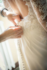 Bridesmaid helping bride with dressing in domestic room