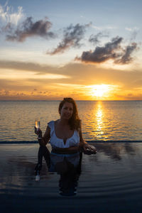 Rear view of woman standing in sea against sky during sunset