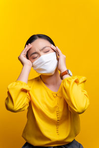 Mid adult woman standing against yellow wall