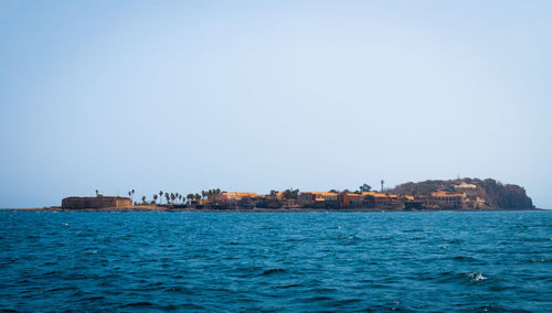 Buildings by sea against clear blue sky