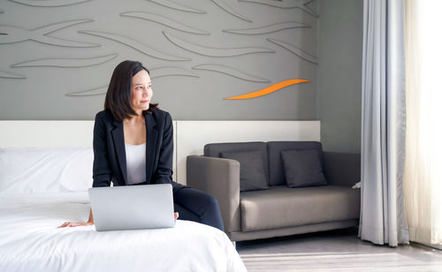 Young woman using phone while sitting on bed
