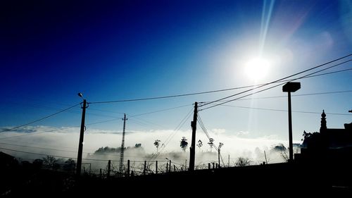 Low angle view of silhouette electricity pylons against blue sky