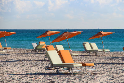 Orange lounge chairs and parasols at beach against sky