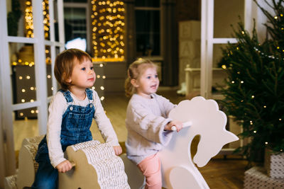 Little children ride toy horses in decorated christmas interior.