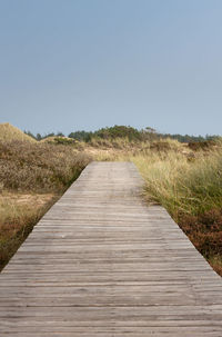 Boardwalk on field against clear sky