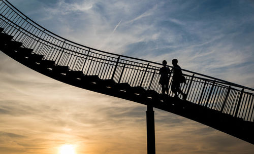 Low angle view of silhouette people standing on footbridge