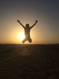 Silhouette man jumping on beach against sky during sunset